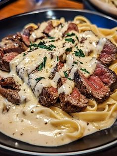 a plate of pasta with steak and sauce on it