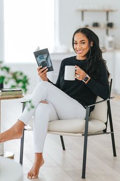 a woman sitting in a chair holding a coffee cup and reading a book