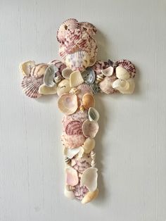 a cross made out of seashells and sea shells on a white wall with a teddy bear in the center