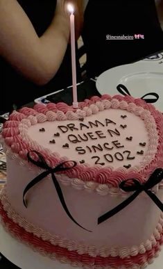 a pink heart shaped cake with a lit candle in the middle that reads drama queen since 2009