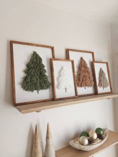 three framed christmas trees are hanging on the wall above a shelf with ornaments and other decorations