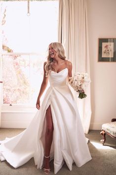 a woman in a white dress is smiling and posing for the camera while holding a bouquet