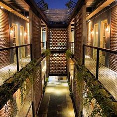 an alley way with lights and plants growing on the walls, between two buildings at night