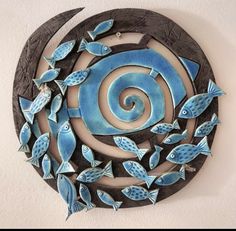 a blue and black circular sculpture with fish on it's side in front of a white wall