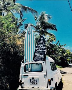 an old van with surfboards on the back parked in front of trees and palm trees