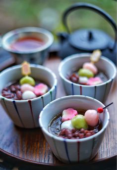 four small bowls filled with food on top of a wooden table next to a teapot