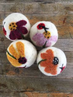 four white balls with flowers painted on them sitting on a wooden surface next to each other