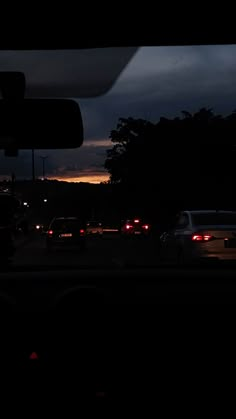 cars are driving down the road at night with dark clouds in the sky behind them