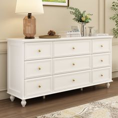 a white dresser with two lamps on top of it and a rug in front of it