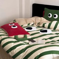 a bed with green and white striped sheets has eyes on it, while two red pillows are in front of the headboard