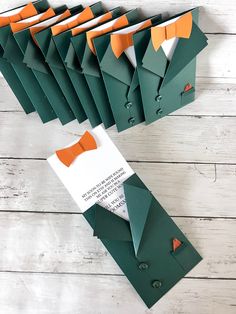 an assortment of folded green and orange paper with bow ties on them sitting on a white wooden surface