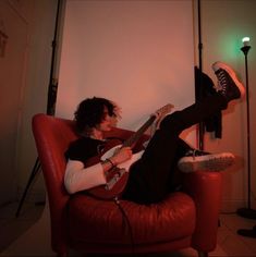 a man sitting in a red chair with his feet up and playing an electric guitar