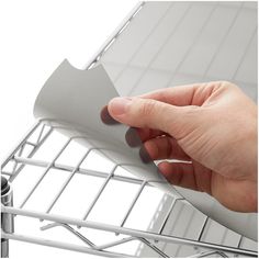 a hand holding a piece of paper on top of a metal rack with wire bars