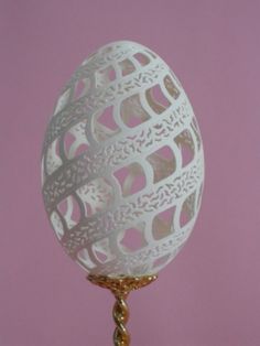 an egg is sitting on a stand against a pink background with gold trimmings