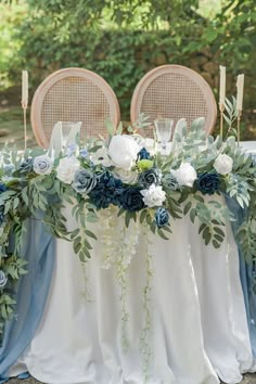 the table is set with blue and white flowers, greenery, candles and napkins