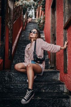 a woman is sitting on the steps in front of red buildings with her arms outstretched