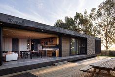 an outdoor kitchen and dining area on a deck with wooden furniture in the foreground