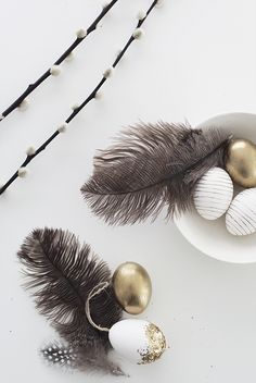 some feathers and eggs in a bowl on a white table with beaded necklaces