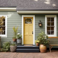 a yellow door sits in front of a gray house with potted plants and chairs