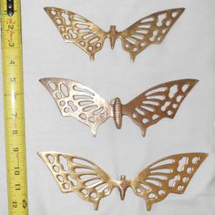 three metal butterflies sitting next to a ruler