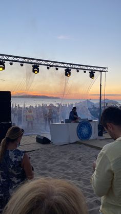 a group of people sitting on top of a sandy beach next to a stage with lights