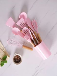 pink kitchen utensils and measuring spoons on a white marble counter with mint leaves