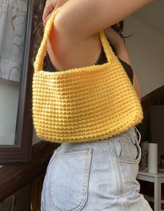 a woman holding onto a yellow crocheted bag in front of a mirror with her hand on her hip