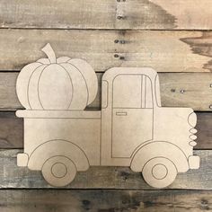 a paper cutout of a truck with a pumpkin on the back, sitting against a wooden wall