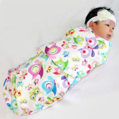 a baby wrapped in a colorful blanket laying on top of a white bed next to a headband