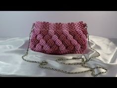 a pink handbag sitting on top of a white cloth covered table next to a silver chain