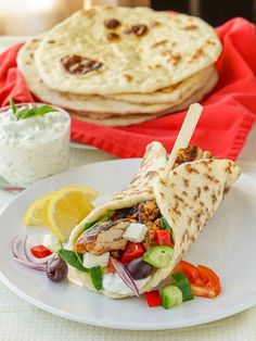 a pita sandwich on a plate next to a bowl of yogurt and lemon wedges