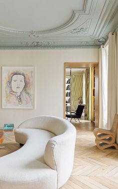 a living room filled with white furniture and paintings on the wall above it's windows