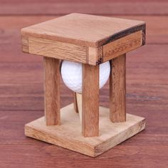 a small wooden object with a golf ball in it's holder on a wood floor