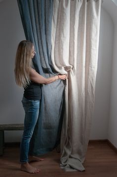 a woman standing next to a curtain in front of a window with the curtains pulled back