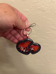 two hearts shaped key chains being held by a person's hand in front of a wall