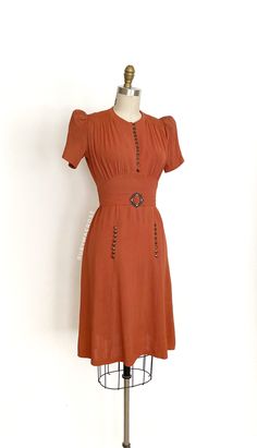 "vintage dress  Era: 1930's Label: none Closure: side metal zipper Material: rayon Colour: cinnamon burnt orangish brown  Details: all the timeless 30's construction details, puff short sleeves with small shoulder pads, decorative skirt buttons, original matching waist belt with buckle Fits like: xsmall / small Bust: 32 - 36\" Waist: 24/25\" Hips: 34 - 36\" Length: 39.5\" Condition: An as is, as found beauty. There is still a vintage smell even after washing it. The buttons are modern but a good match with the vintage buckle. There are inconsistencies in the colour throughout the dress. There are spots and marks on the skirt. Some ares of discolouration at the waist and on the back of the bodice. There are some tiny holes at the back shoulder area.  Priced accordingly.   shop policy  * All 1940s Shirtwaist Dress, 1930s Summer Dress, Brown Knee-length Vintage Dress, Vintage Brown Short Sleeve Dress, Brown Vintage Short Sleeve Dress, 30s Outfits Vintage 1930s Fashion, 1930s Womens Fashion, 1930s Day Dress, 30s Outfits