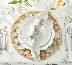 a place setting with white plates, silverware and green floral napkins on a wicker plate