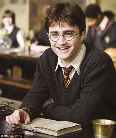 a young man sitting at a table in front of a book and some cups on it