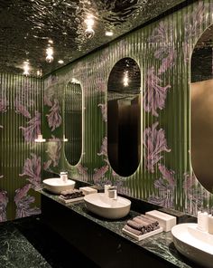 two sinks and mirrors in a bathroom with green wallpaper on the walls, along with other fixtures