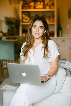 a woman sitting on a couch with a laptop computer in her lap and looking at the camera