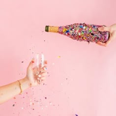 two hands holding candles and confetti on a pink background with sprinkles