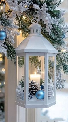 a white lantern hanging from a christmas tree with blue ornaments and pine cones on it