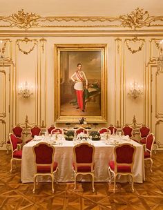 a painting is hanging in the middle of a dining room with red chairs and white tablecloths