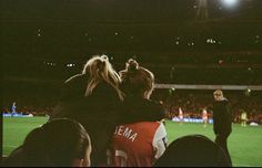 two people sitting on the back of a woman's shoulders at a soccer game