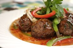 some meatballs and vegetables are on a white plate with sauce in the middle that is drizzled over them