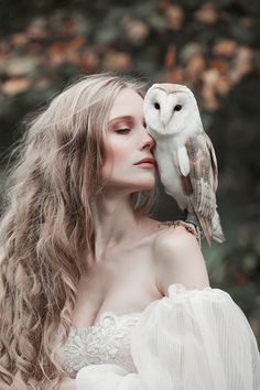 a woman in white dress holding an owl on her shoulder