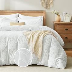 a bed with white comforter and pillows on top of it next to a dresser