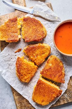 grilled cheese sandwiches cut in half on a cutting board next to a bowl of tomato soup