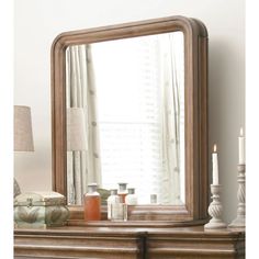 a mirror sitting on top of a wooden dresser next to a lamp and table with candles