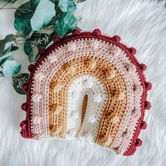 a crocheted pot holder with a rainbow shaped hole in the middle on a white rug